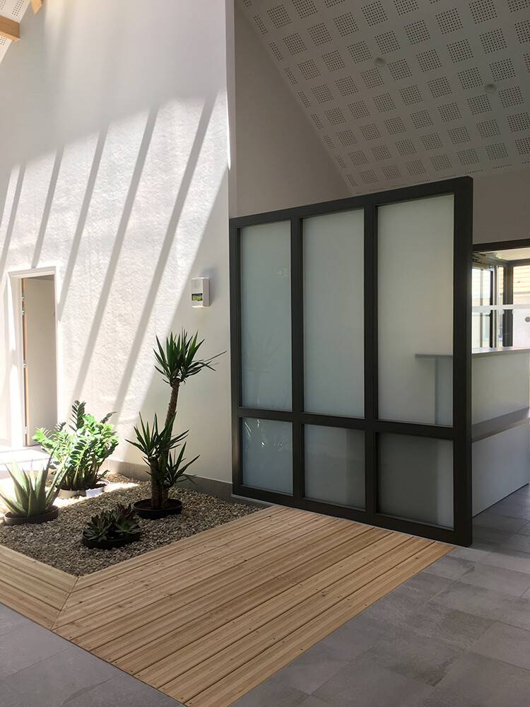 Hall d'accueil avec verrière noire et terrasse bois intérieure