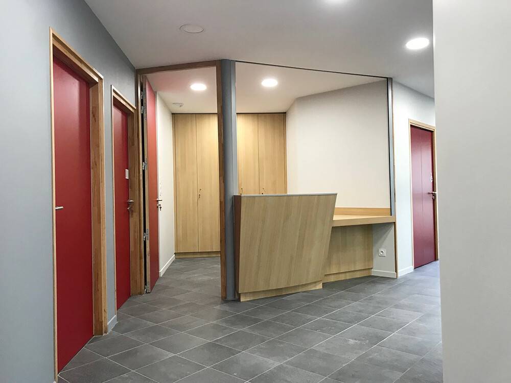 Accueil de cabinet médical avec banque d'accueil bois et portes rouges