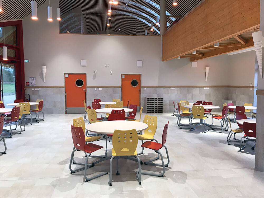Salle de restauration scolaire avec tables rondes et chaises colorées