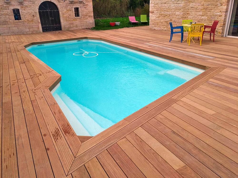 Plage de piscine en bois exotique devant maison en pierre