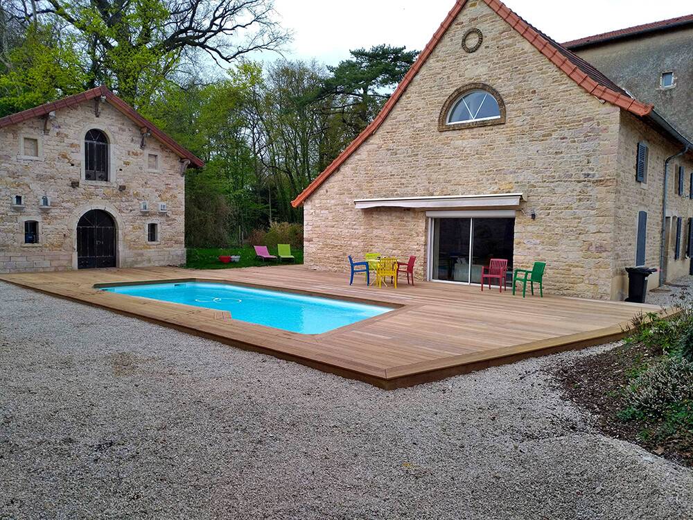 Terrasse bois autour d'une piscine devant maison en pierre